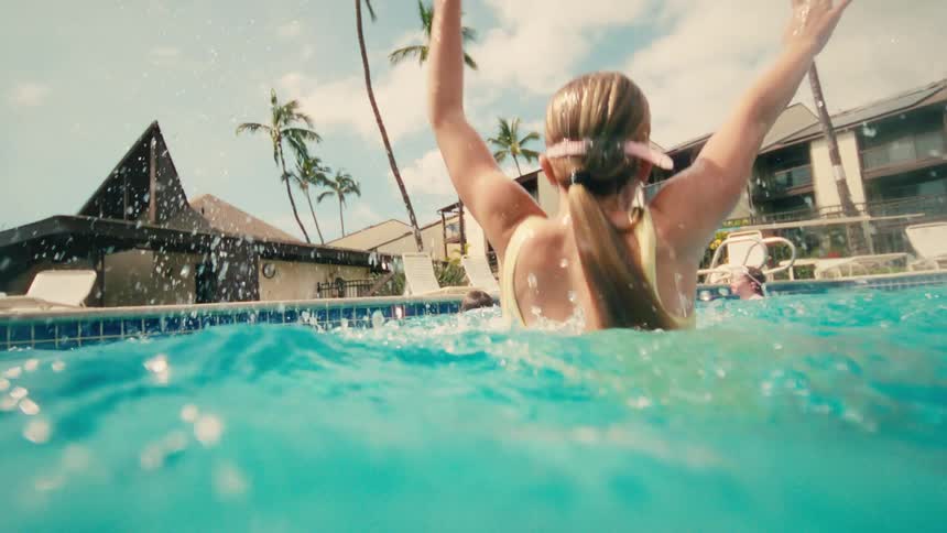 Slow motion split-level shot of two children joyfully splashing and swimming in a tropical resort pool