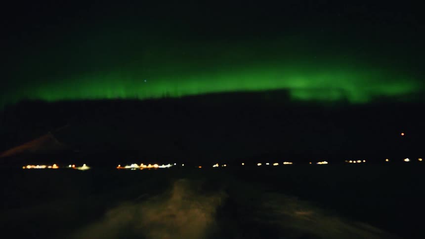 A point-of-view shot from a moving vehicle driving across a snowy landscape at night under the beautiful green glow of the Aurora Borealis