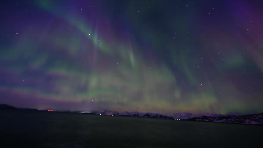 A spectacular timelapse captures the vibrant green and purple Aurora Borealis dancing across the starry night sky into dawn over a snowy Norwegian fjord