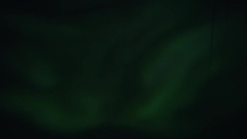 The stunning green Aurora Borealis swirls and dances in the dark night sky over a quiet, snowy mountain village
