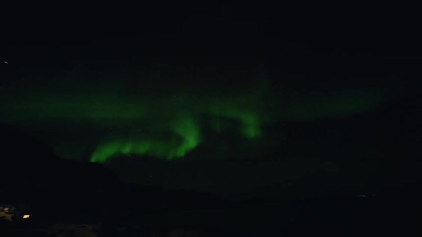 A mesmerizing time-lapse captures the vibrant green Northern Lights dancing and swirling in the night sky above a remote mountain village
