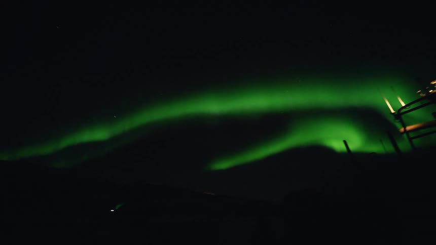 A slow pan reveals the mesmerizing green bands of the Aurora Borealis dancing in the dark night sky
