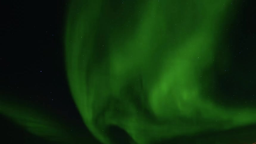 Vibrant green ribbons of the Aurora Borealis dance and wave across a clear, starry night sky in a stunning time-lapse