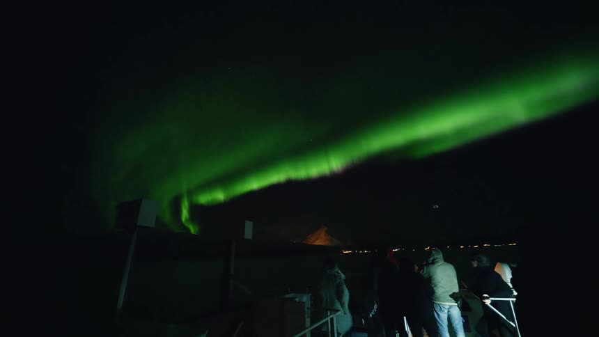 Tourists stand in awe as the Aurora Borealis illuminates the dark night sky with a spectacular green glow