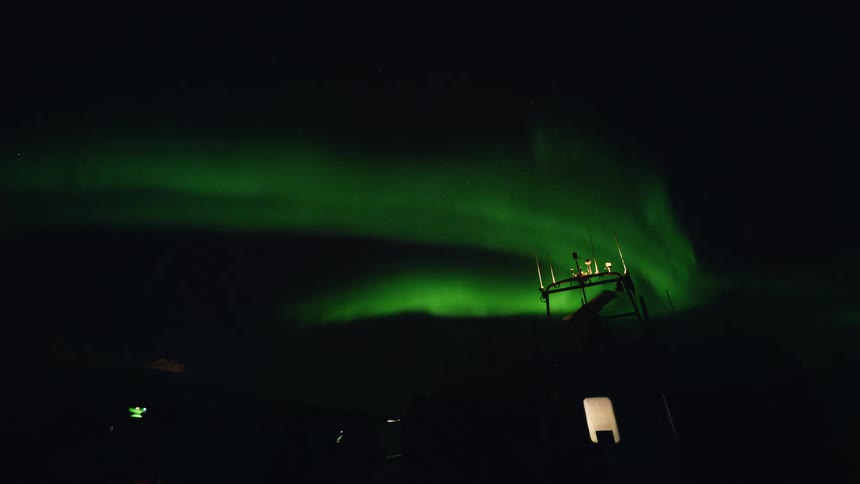 A vibrant green Aurora Borealis dances across the night sky above a remote scientific monitoring station