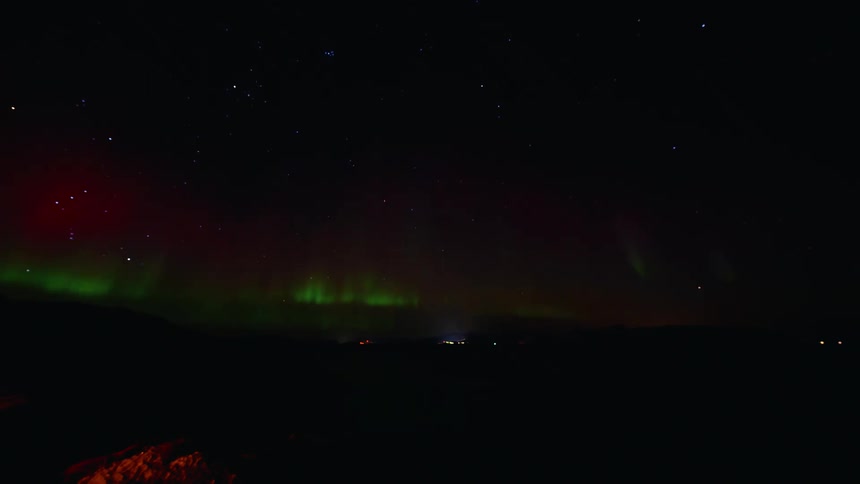 A mesmerizing time-lapse of the vibrant green and red Northern Lights dancing across the starry night sky over a calm body of water