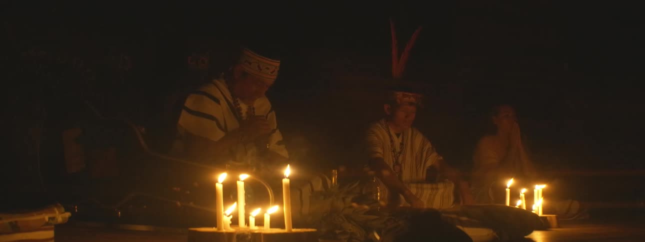 Indigenous shamans perform a sacred candlelit ritual in a dark, spiritual setting