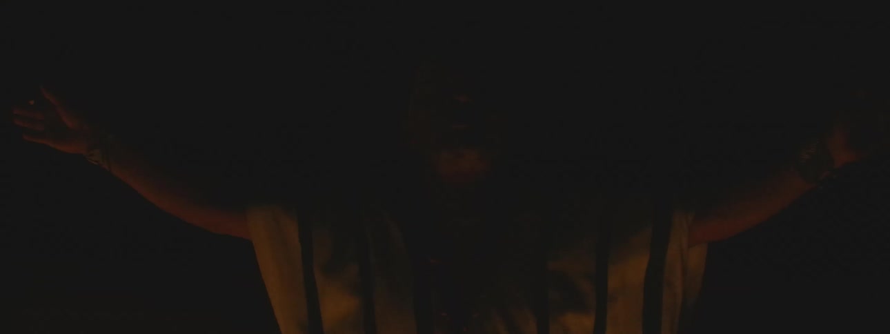 A shaman smokes a ceremonial cigar and performs a sacred ritual in the dark, illuminated by the glow of a fire