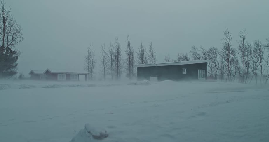 Remote houses stand against a fierce blizzard as strong winds whip snow across the desolate landscape