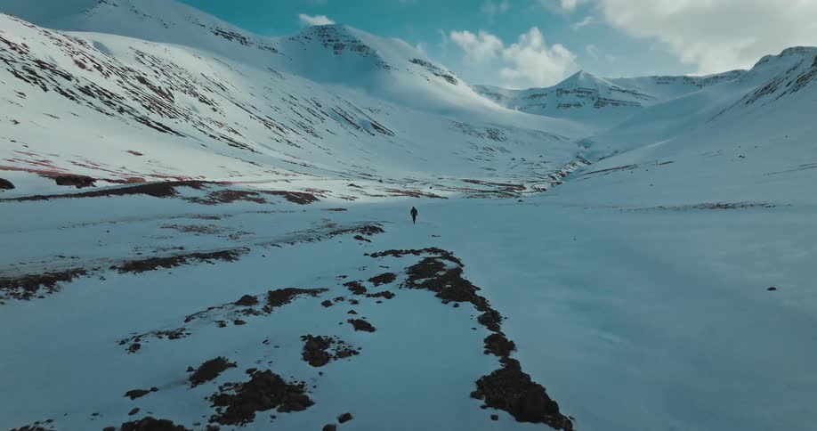Aerial view of a solitary figure hiking through a majestic, snowy mountain landscape