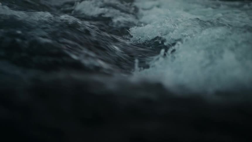 Dark, turbulent water churns and flows in a powerful slow-motion close-up