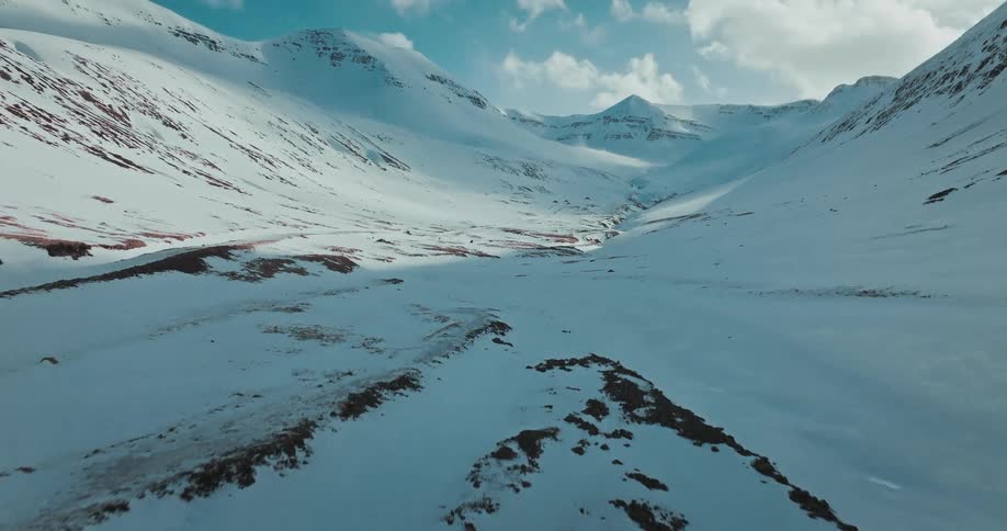 An aerial view follows a lone hiker as they trek through a vast and majestic snow-covered mountain valley