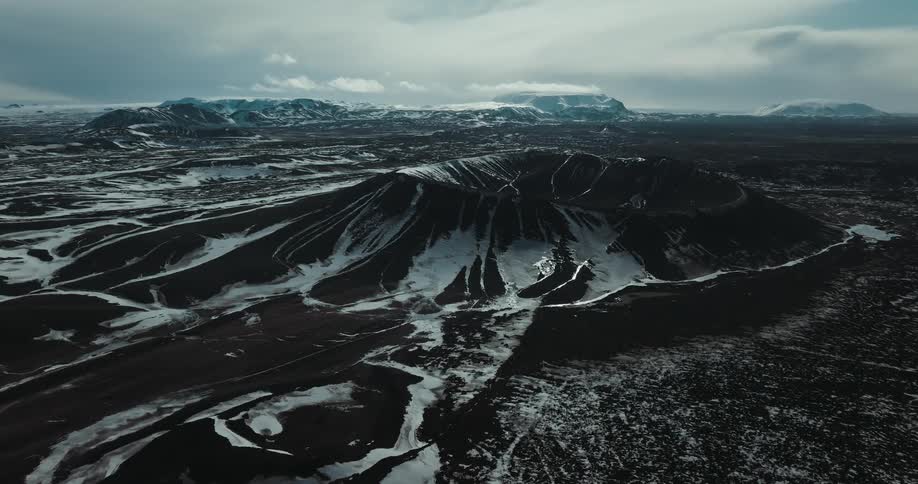 A slow aerial pullback reveals a vast, snow-dusted volcano crater in a desolate Icelandic landscape
