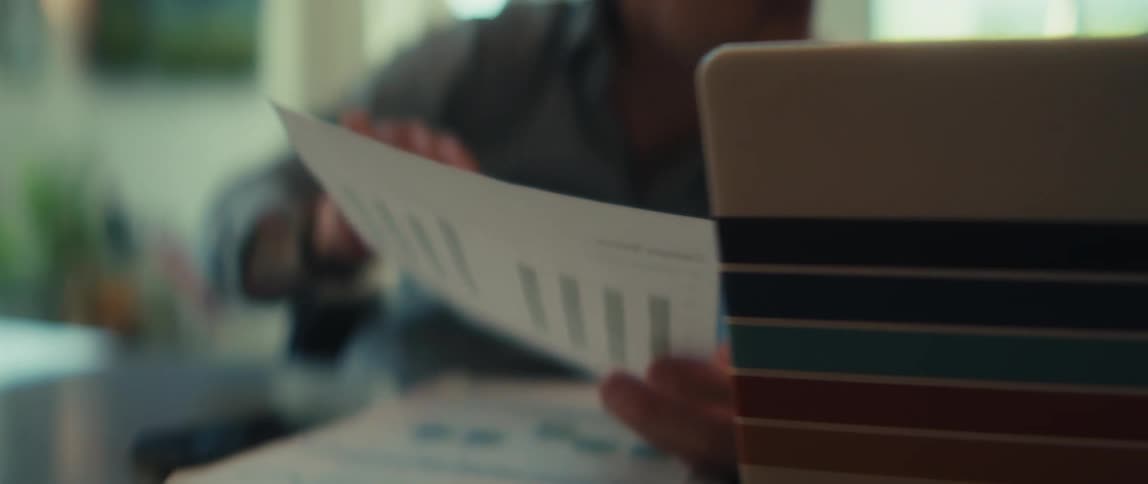A business professional studies a printed report with a bar graph while working at a desk in a modern office