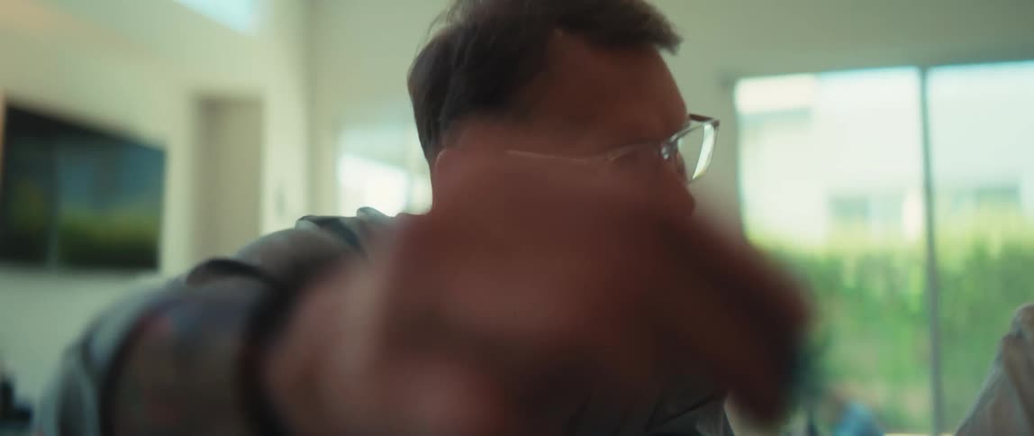 A man with glasses uses a pen to explain something on a laptop to a woman as they work together in a modern home