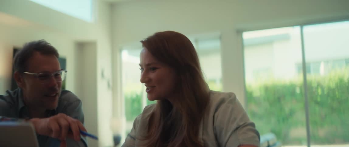A happy couple smiles while collaborating on their finances with a laptop in their modern sunlit kitchen