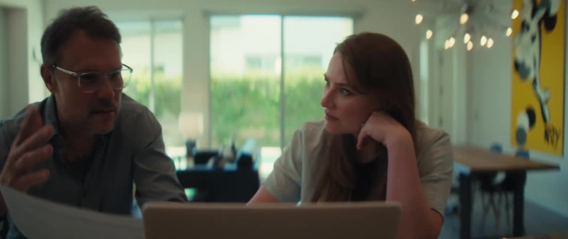 A man with tattoos on his arm explains business plans to a female colleague during a meeting in a bright, modern office
