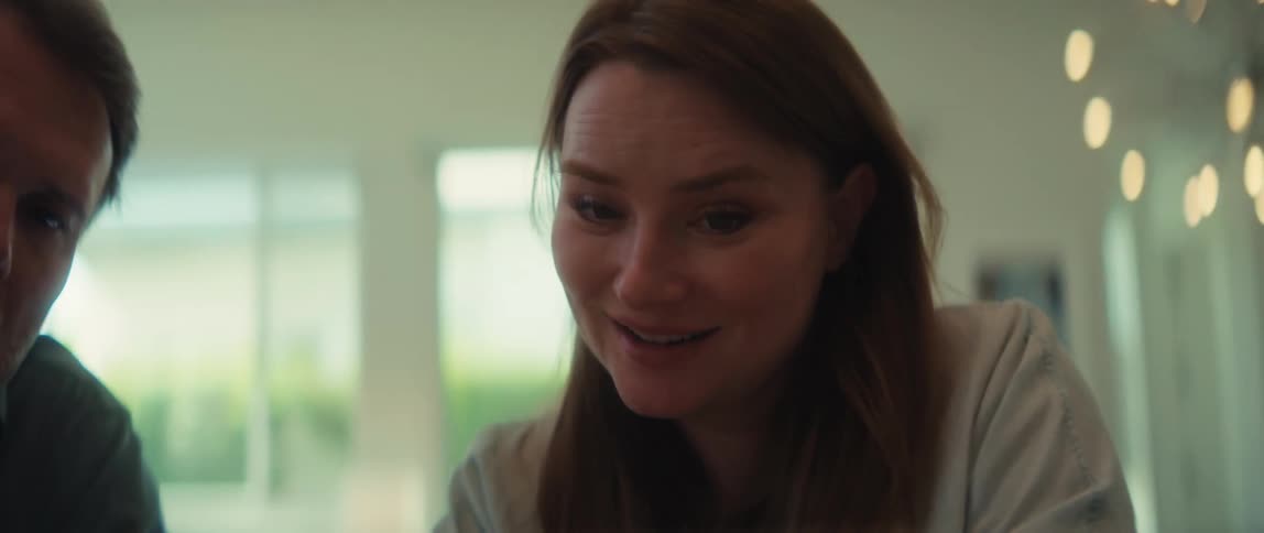 A concerned woman's face breaks into a happy smile as she and her partner review something together at home