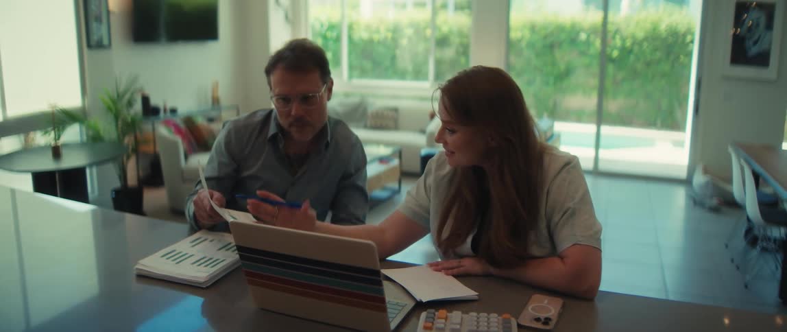 A man and woman review business documents with charts and graphs on a laptop at their home office