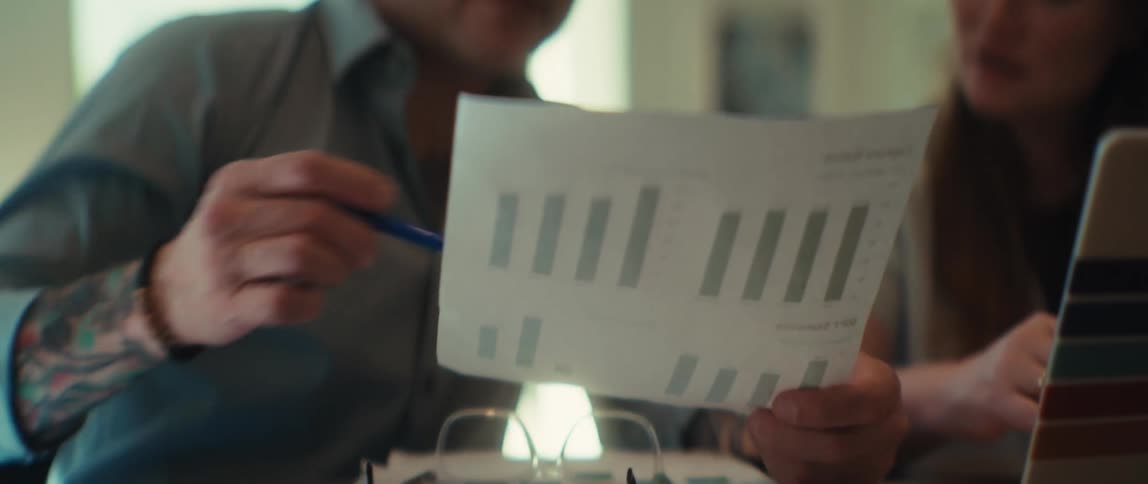 A tattooed businessman and his female colleague analyze a business report with bar charts during a meeting