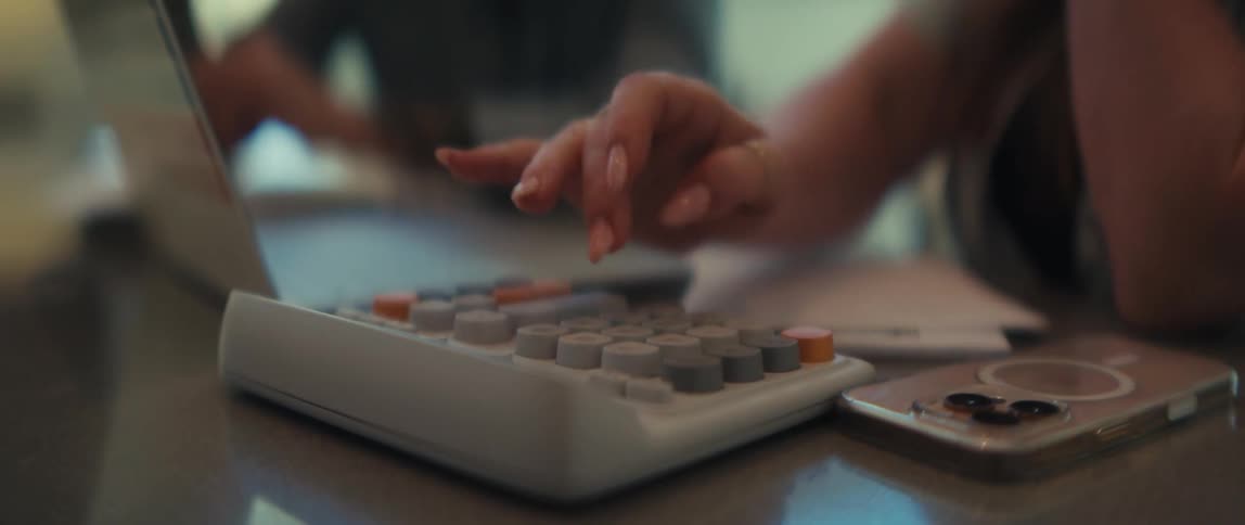A close-up, slow-motion shot of a woman's manicured hand calculating numbers on a modern calculator during a business meeting