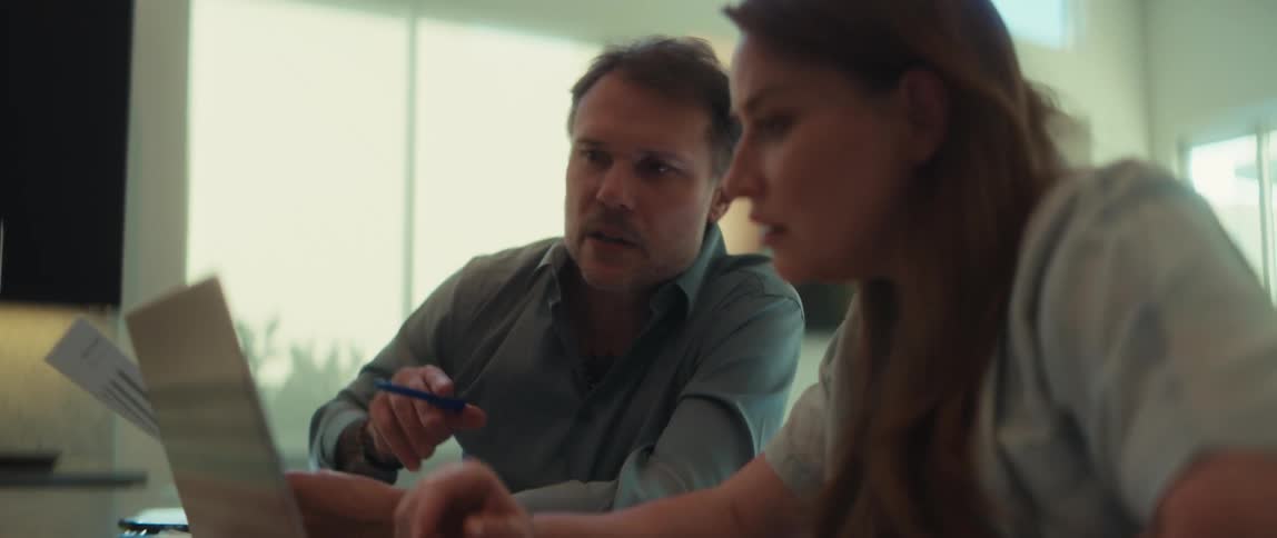 A senior male mentor guides his female colleague on a project, pointing to a laptop screen in a bright office