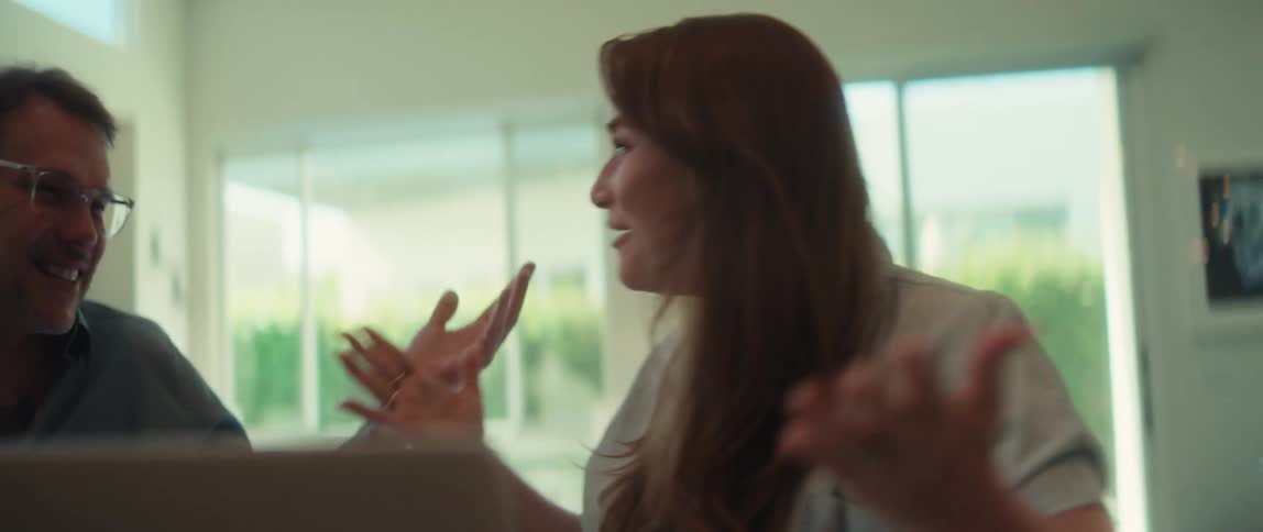 An excited couple celebrates good news with a high-five while working on a laptop at their modern kitchen island