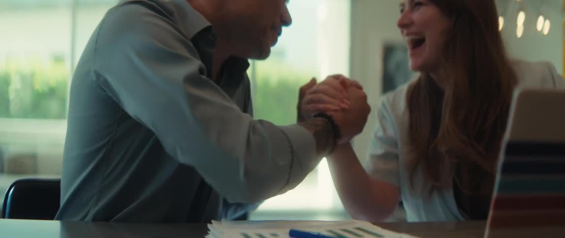 Two happy coworkers take a playful break from work to arm wrestle at the table in slow motion