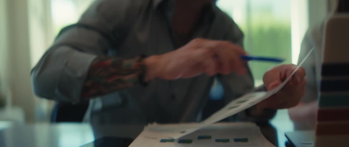 A tattooed businessman with glasses smiles as he explains a business report during a meeting in a modern office