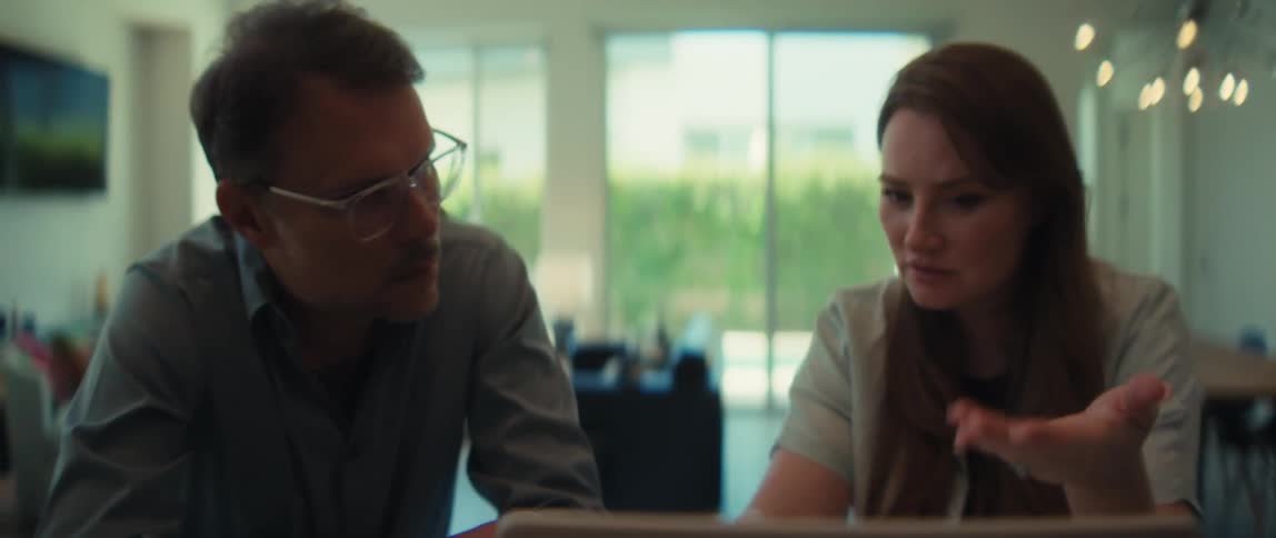 A man and woman collaborate on a business project, intently focused on a screen in a modern, sunlit office