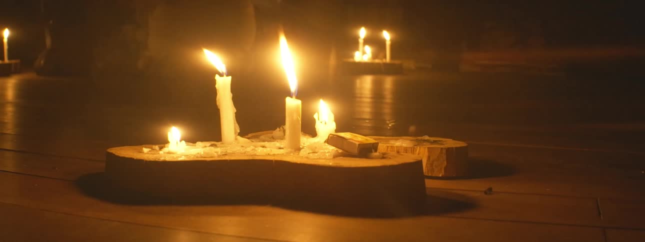 Flickering candles on wooden holders cast a warm, intimate glow in a dark room