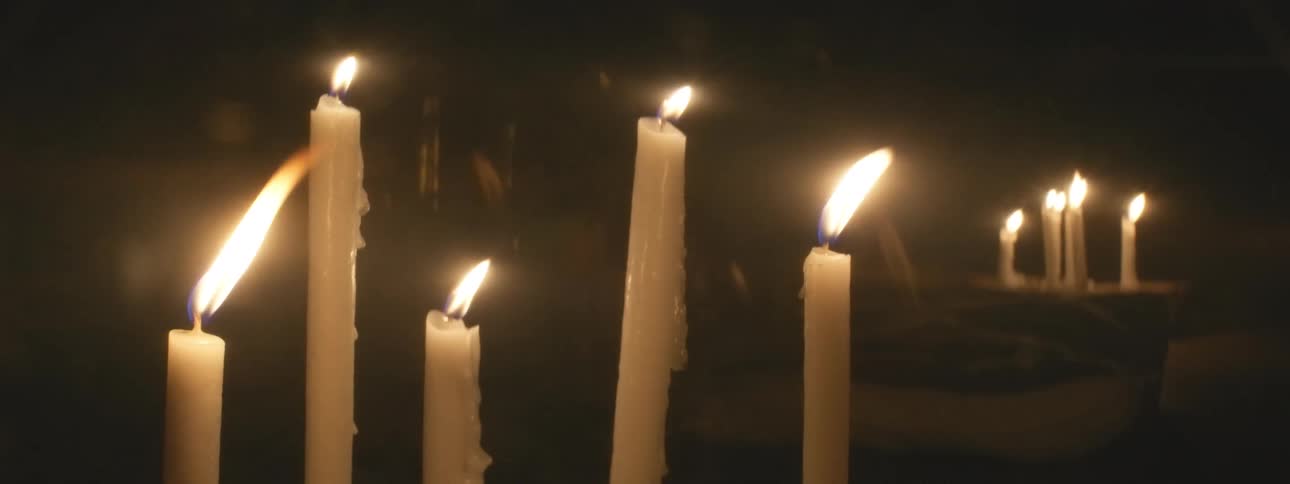 A close-up view of multiple white taper candles flickering in the darkness