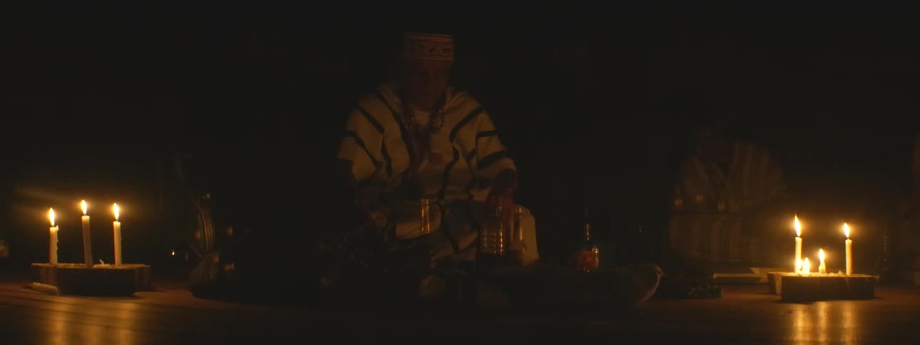 An indigenous shaman in traditional clothing performs a spiritual ceremony by candlelight