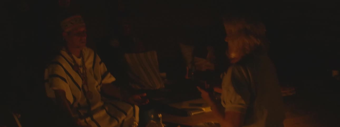 A shaman in traditional robes conducts a mystical candlelit ceremony with a group of followers at night