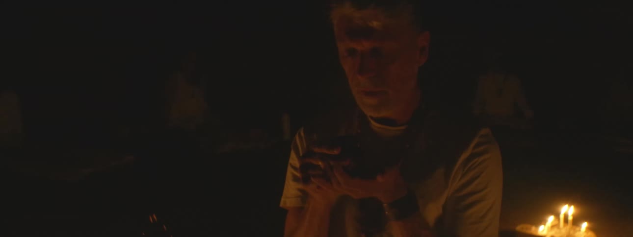 A spiritual leader drinks from a ceremonial cup during a sacred ritual by candlelight