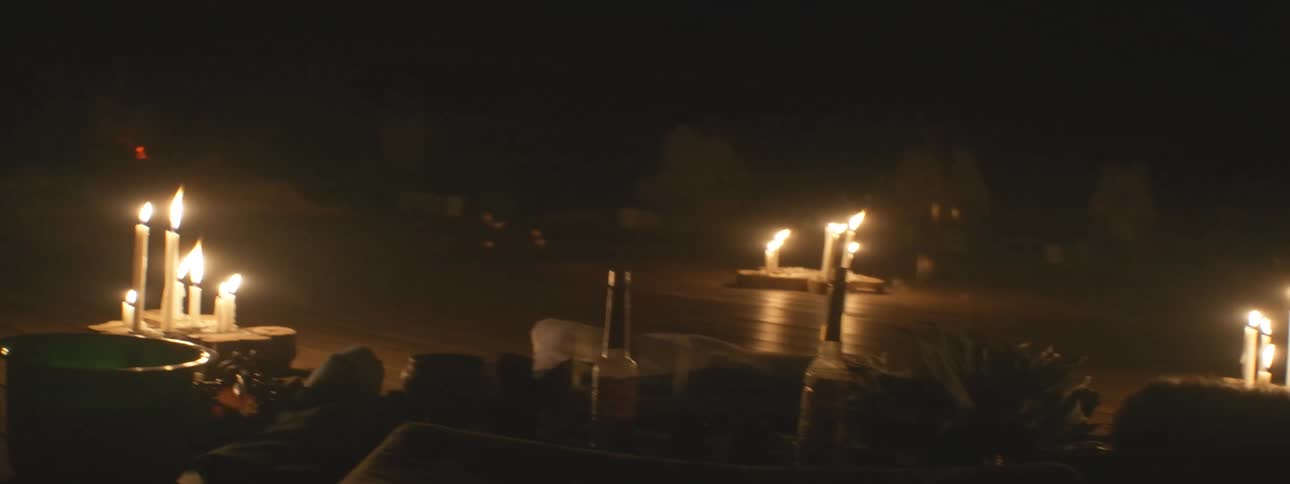A slow panning shot across a dark room reveals a spiritual ceremony taking place by candlelight