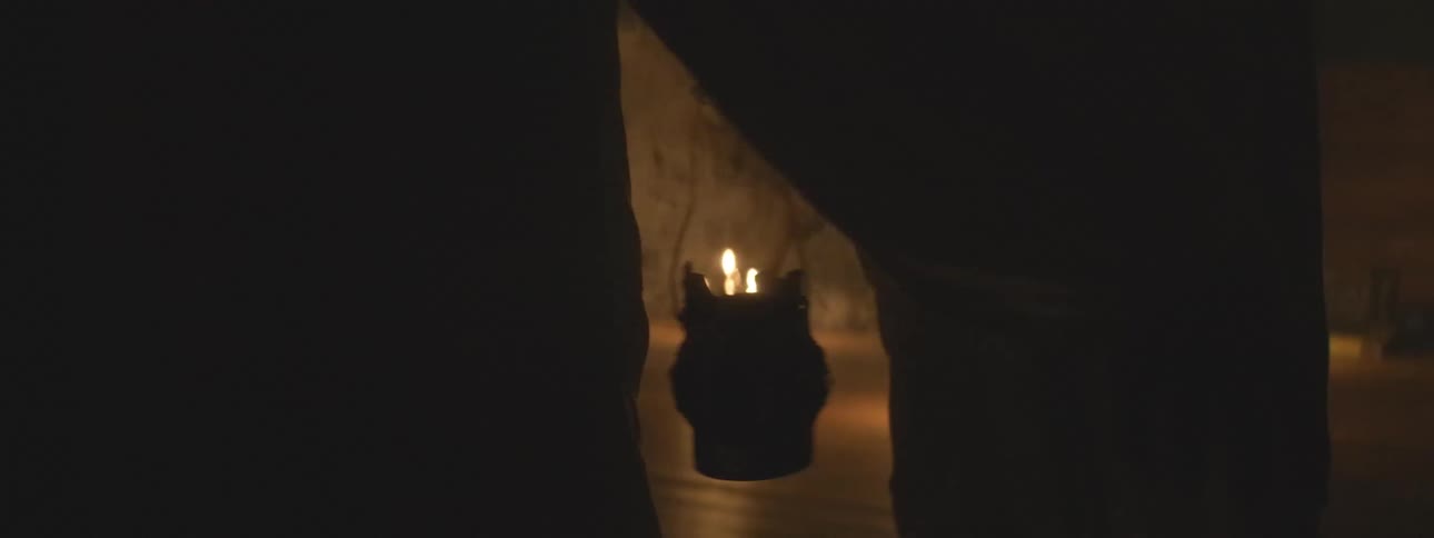 Following a silhouetted figure through a dark, smoky room during a candlelit spiritual ceremony
