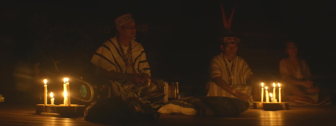 Indigenous shamans lead a sacred spiritual ceremony in a dark room illuminated by flickering candlelight