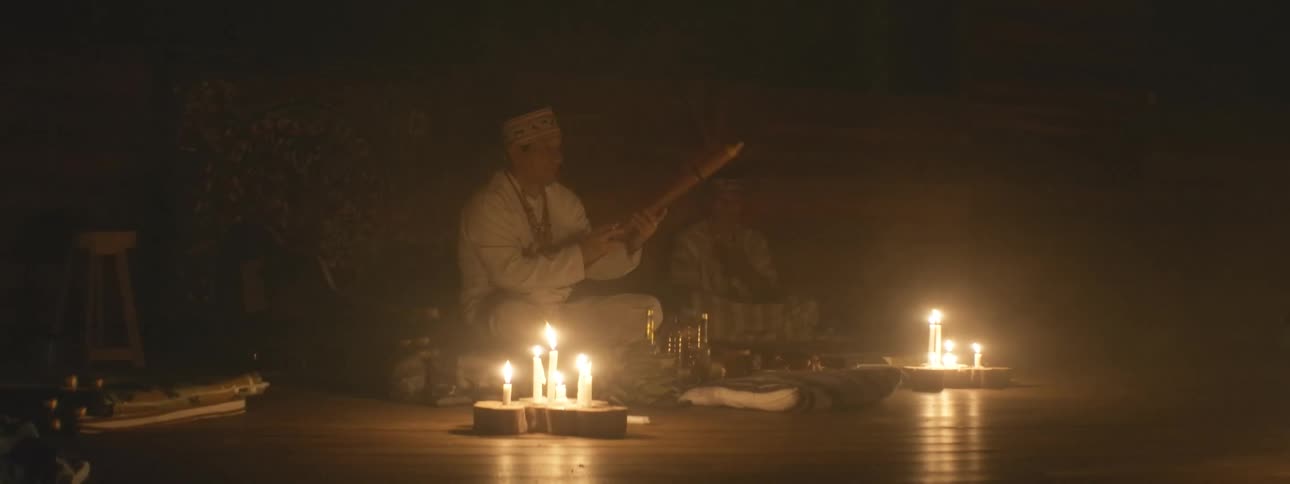 A spiritual leader conducts a traditional ceremony, smoking and blessing a ritual object surrounded by candlelight