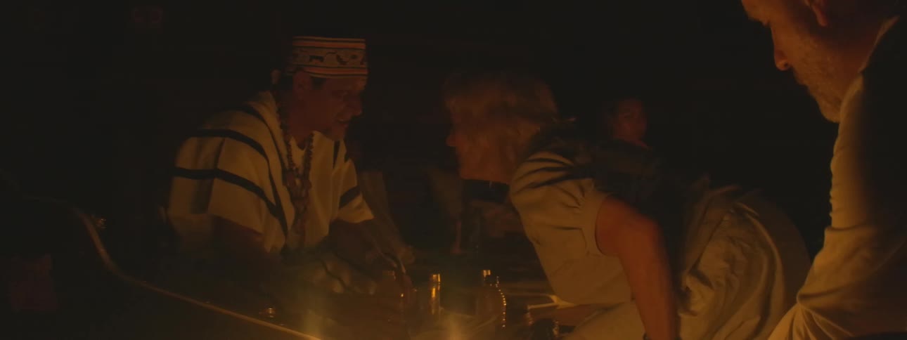 An indigenous shaman leads a traditional spiritual ceremony with participants in a dark, candle-lit room