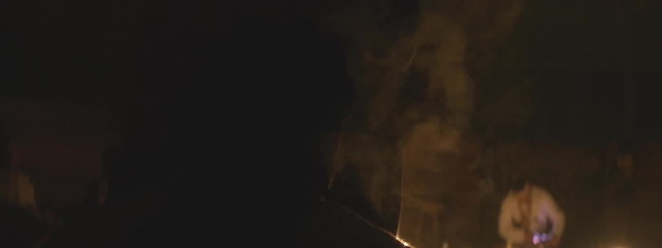 A mysterious and somber historical gathering unfolds in a dark, smoky room illuminated by flickering candlelight
