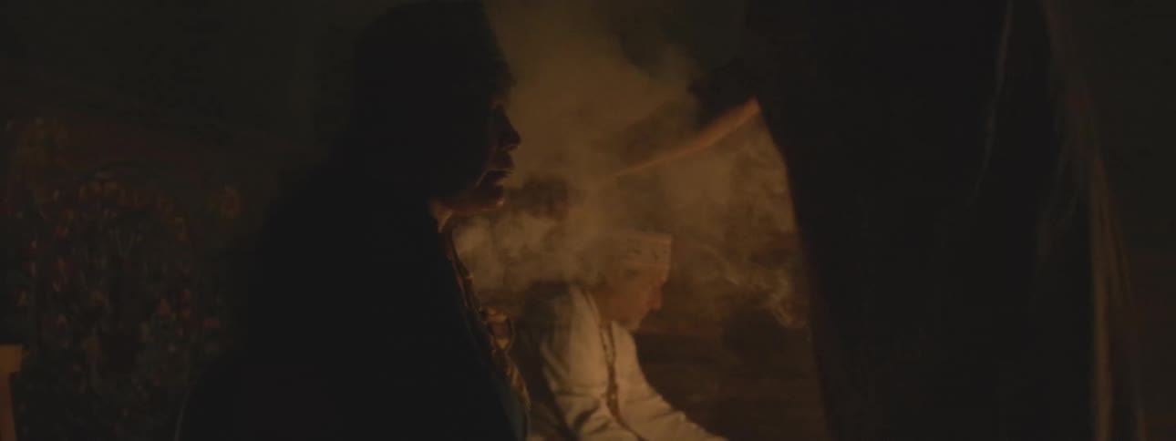 A shaman performs a sacred ritual with burning incense and candles in a dark, smoke-filled room