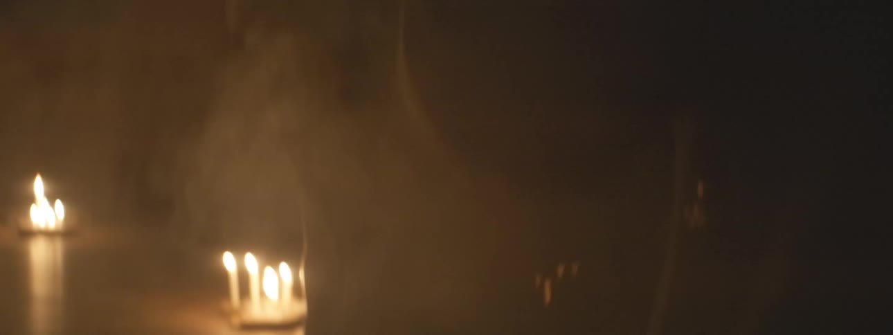 A mysterious and spooky candlelight ritual with silhouetted figures dancing in a smoke-filled room