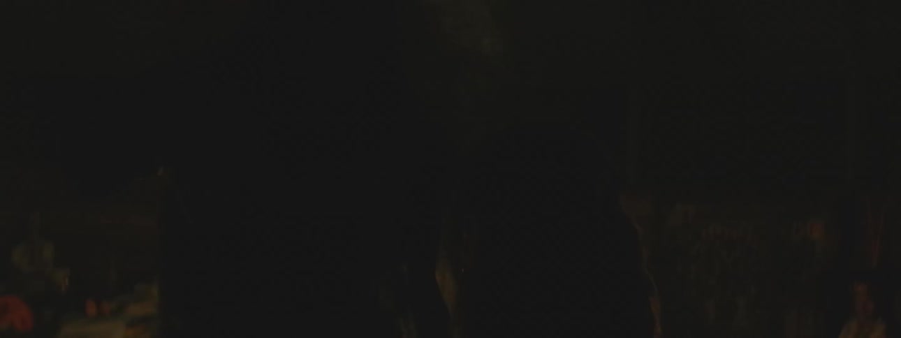Silhouettes of people gathered around candles during a sacred nighttime ceremony with incense smoke filling the room