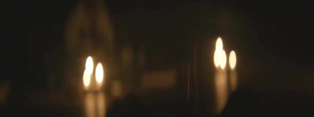 Mysterious silhouettes move through a dark, candlelit space in a blurry, atmospheric shot