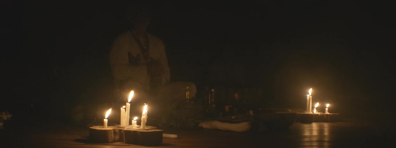 A shaman performs a spiritual ritual in a dark room, surrounded by the warm glow of flickering candles and thick smoke