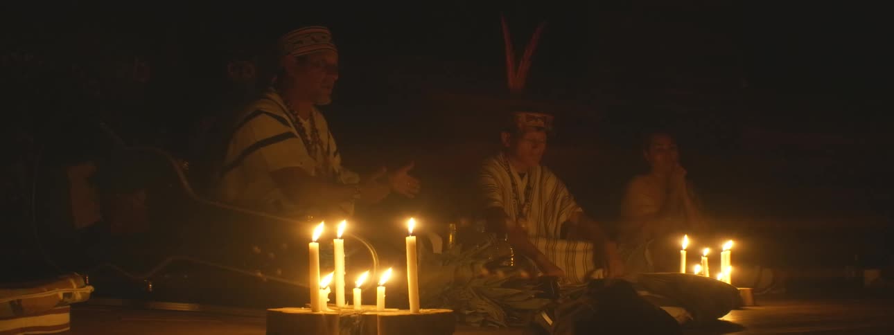 Indigenous shamans lead a spiritual ceremony with chanting and drumming in a dark room illuminated by many candles