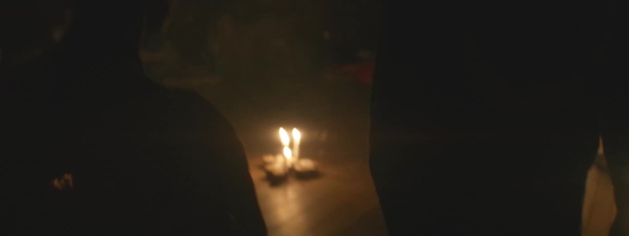 A person's silhouette lights candles on the floor of a dark, smoky room during a spiritual ceremony as the camera slowly reveals the scene