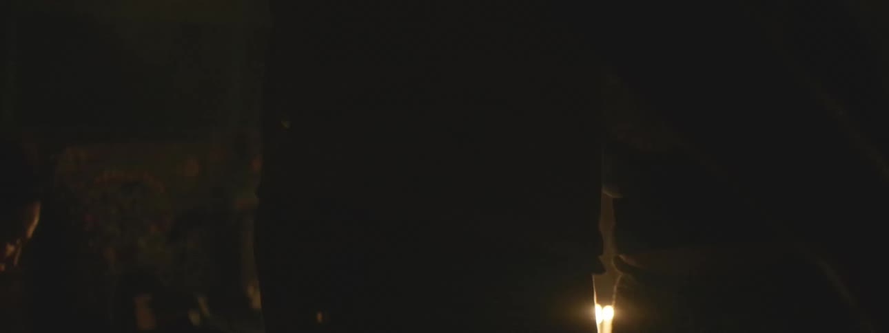 A mysterious spiritual ritual unfolds in a dark, smoky room as a silhouetted figure swings a censer over candles