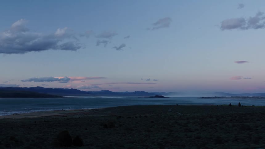 A serene side-scrolling view of a vast mountain lake at twilight, seen from a moving perspective